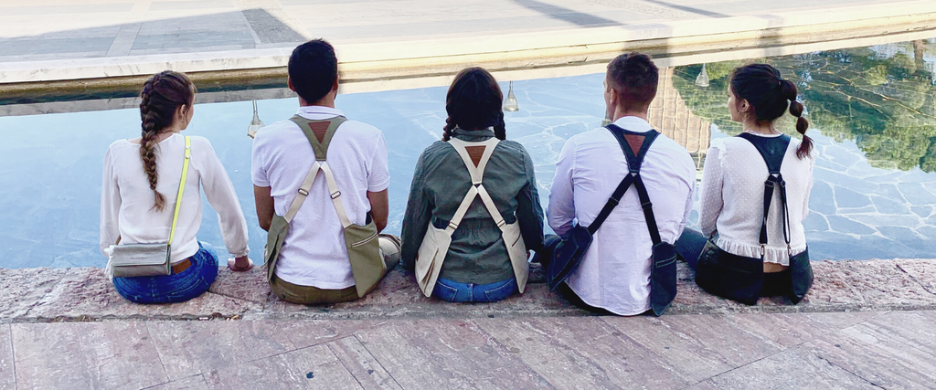 Vista trasera de grupo de amigos que llevan Movers Bag sentados en el borde de una fuente en la plaza de Colón