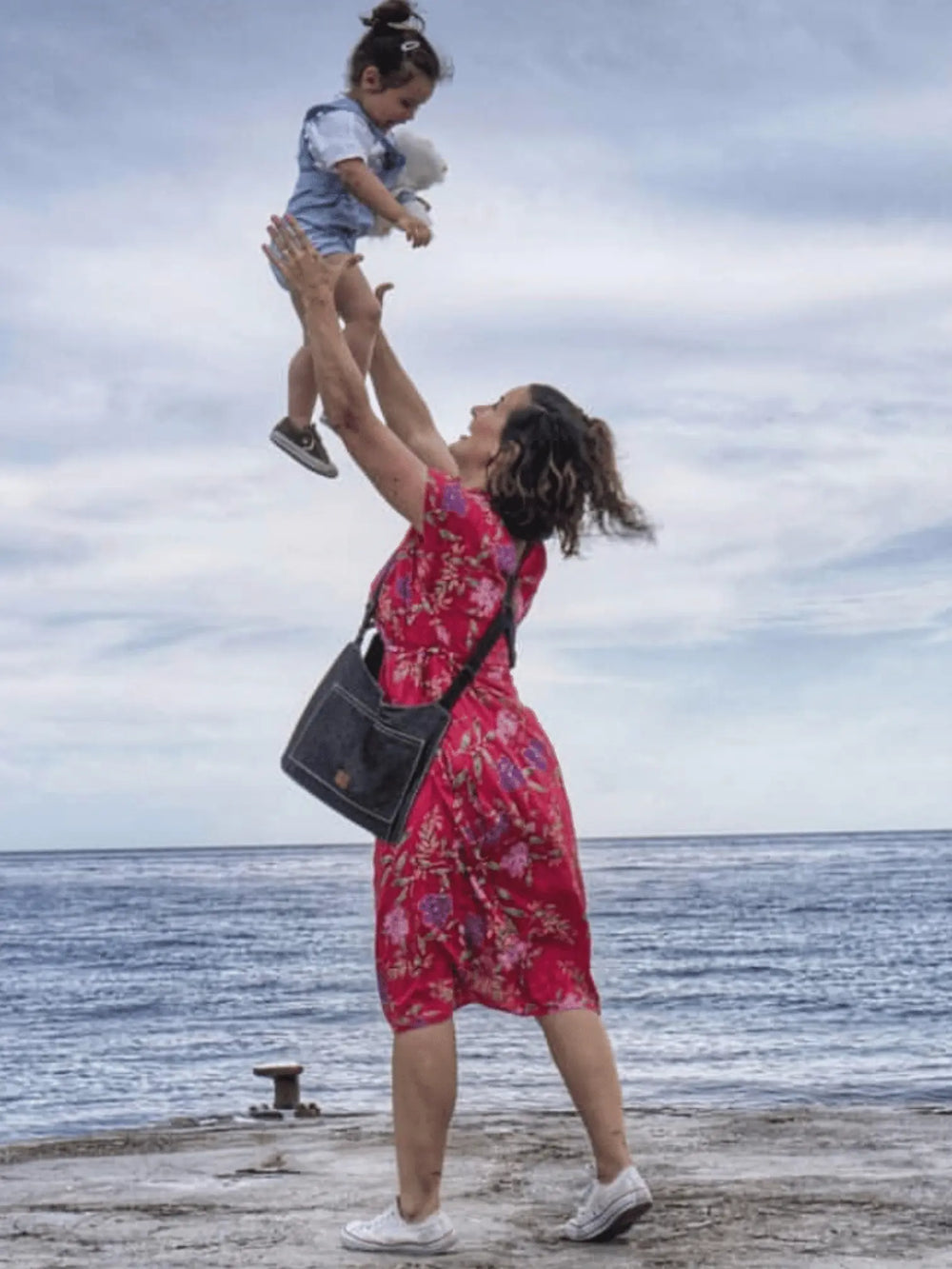 Madre que tirando a su hija el cielo llevando un bolso doble que le permite tener las manos libres