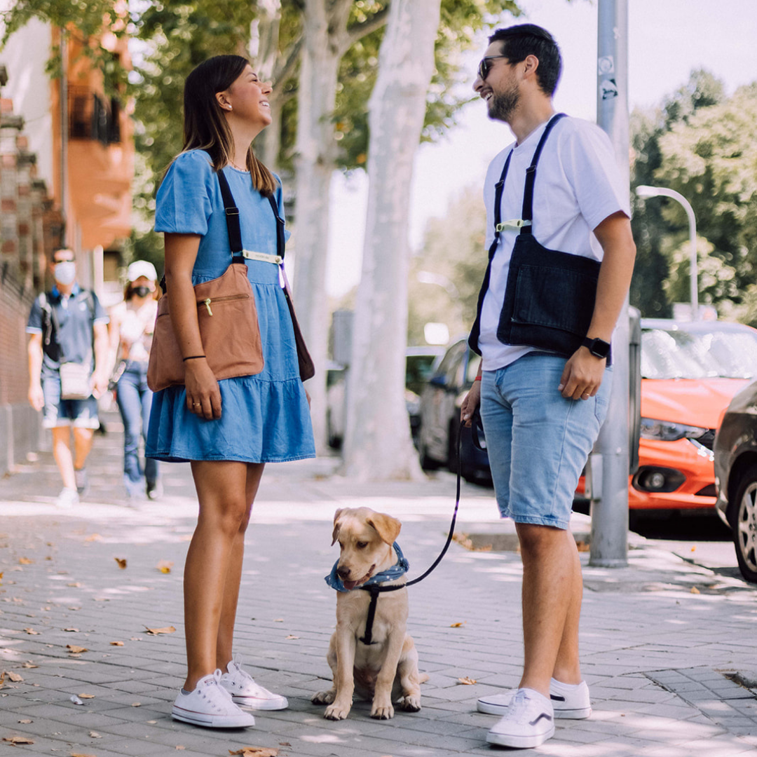 Ejemplo de uso del bolso marrón negro, chica paseando a su perro con el bolso puesto y chico que la acompaña con el bolso negro